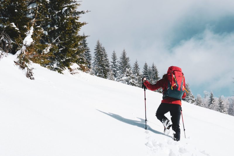 A beautiful shot of a male hiker with a red travel backpack hiking up a snowy mountain in winter